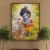 Baby Krishna with cows framed wall art displayed on outdoor garden wall with plants, devotional Krishna illustration.