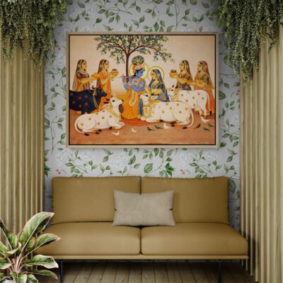 Large framed Pichwai style Radha Krishna artwork above beige sofa with floral wallpaper and indoor plants.